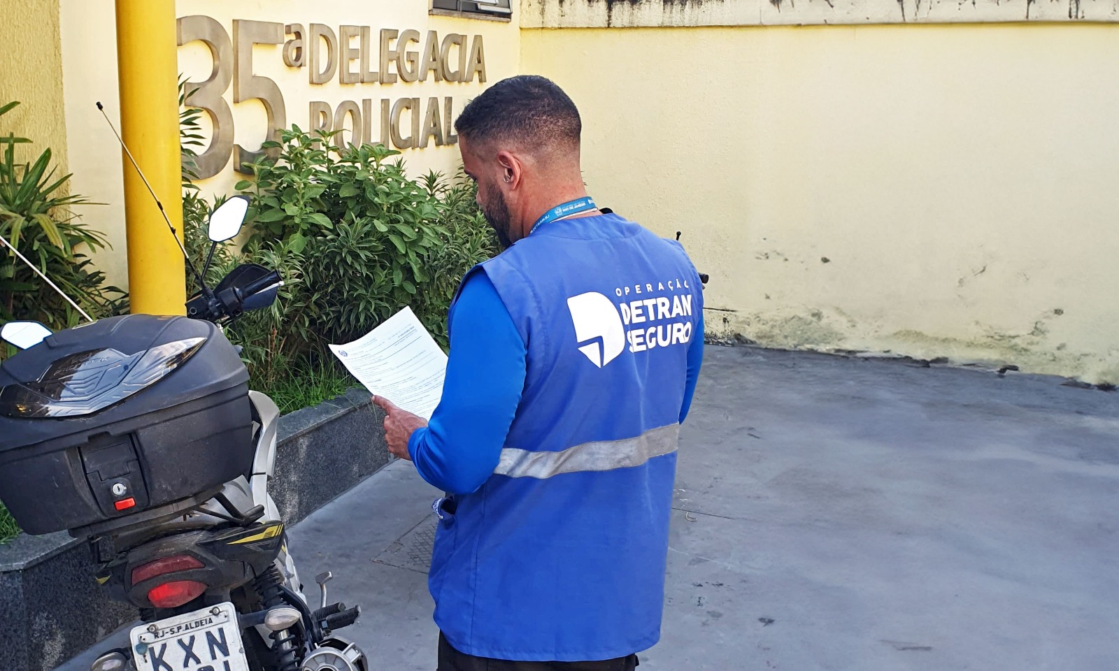 agente de fiscalização do Detran lê documento ao lado de moto apreendida no pátio da 35ª Delegacia de Polícia