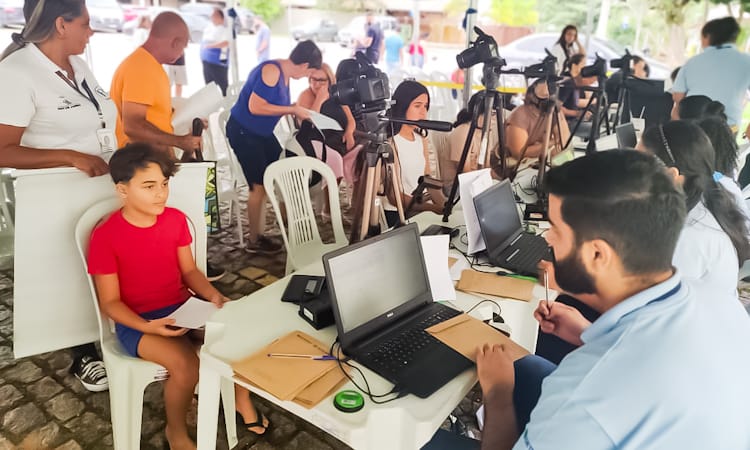 Um menino e uma adolescente tiram fotos para fazer carteira de identidade em evento organizado em área pública