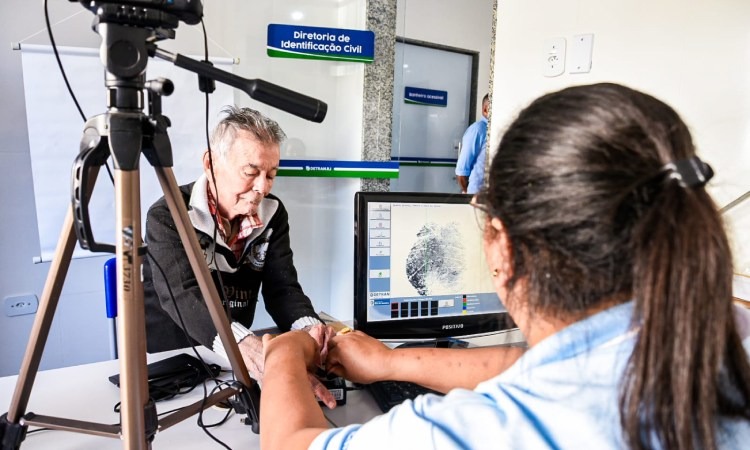 Funcionária do Detran atendendo homem, que tira foto para carteira de identidade em Posto do Detran 