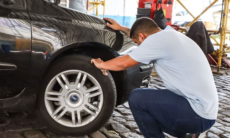 Homem verifica pneu de carro dentro do Posto do Detran