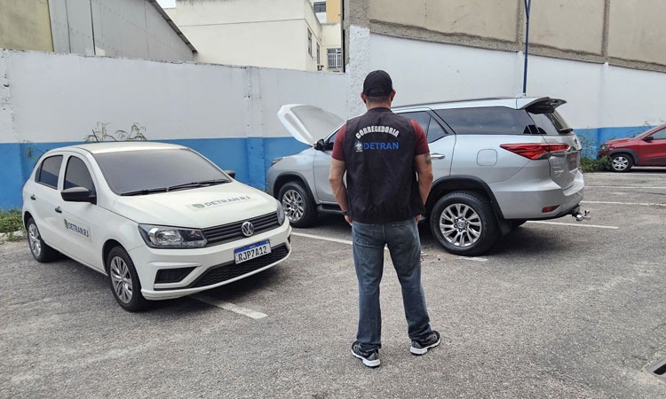 agente  do Detran em frente a dois veículos 